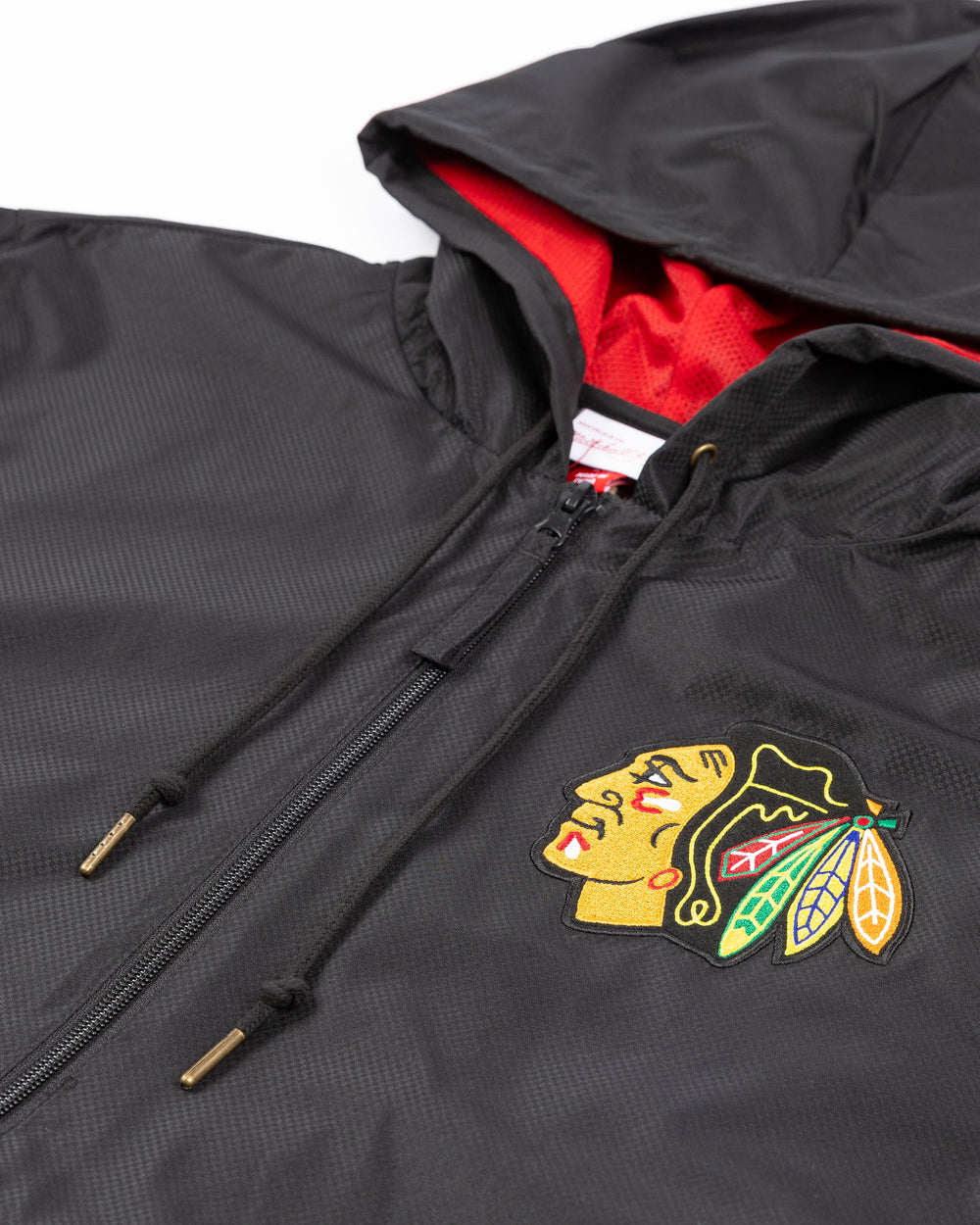 black Mitchell & Ness windbreaker jacket hoodie with Chicago Blackhawks primary logo embroidered on left chest  front detail lay flat