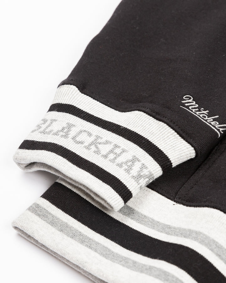two tone black and grey Mitchell &amp; Ness hoodie with Chicago Blackhawks wordmark and primary logo on front - cuff detail lay flat